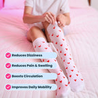 Woman wearing white compression socks with red heart patterns on bed